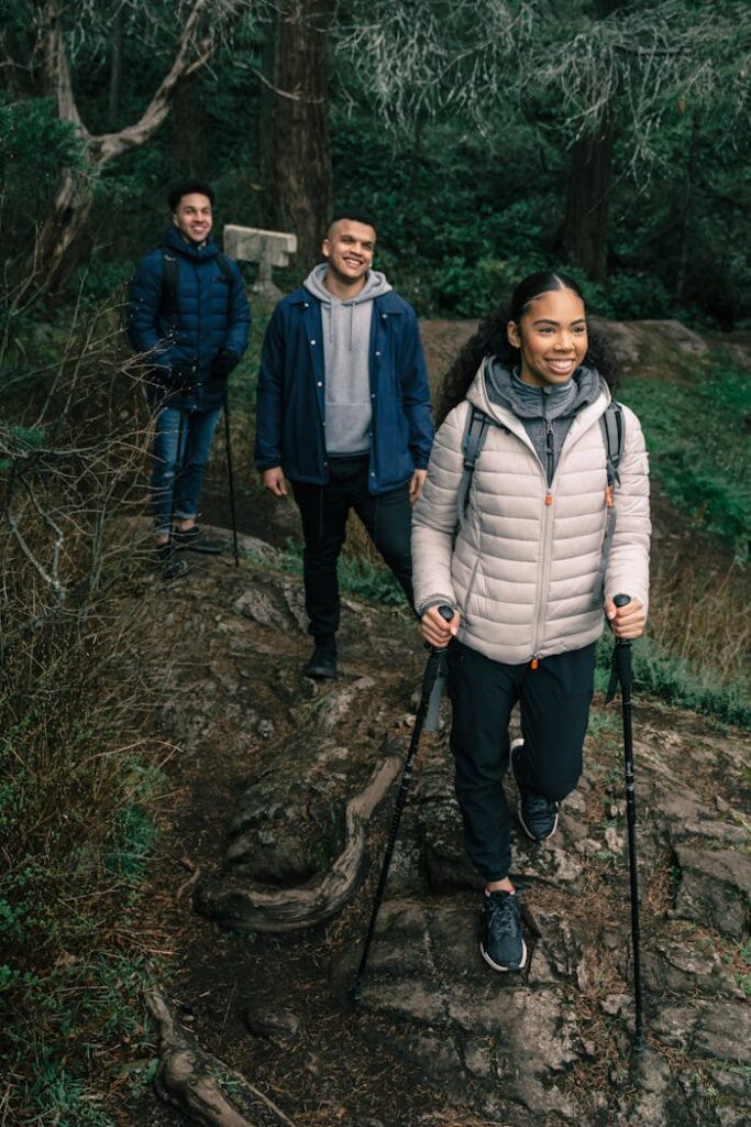 Group of diverse friends enjoying a hike through a lush forest, smiling and using trekking poles.